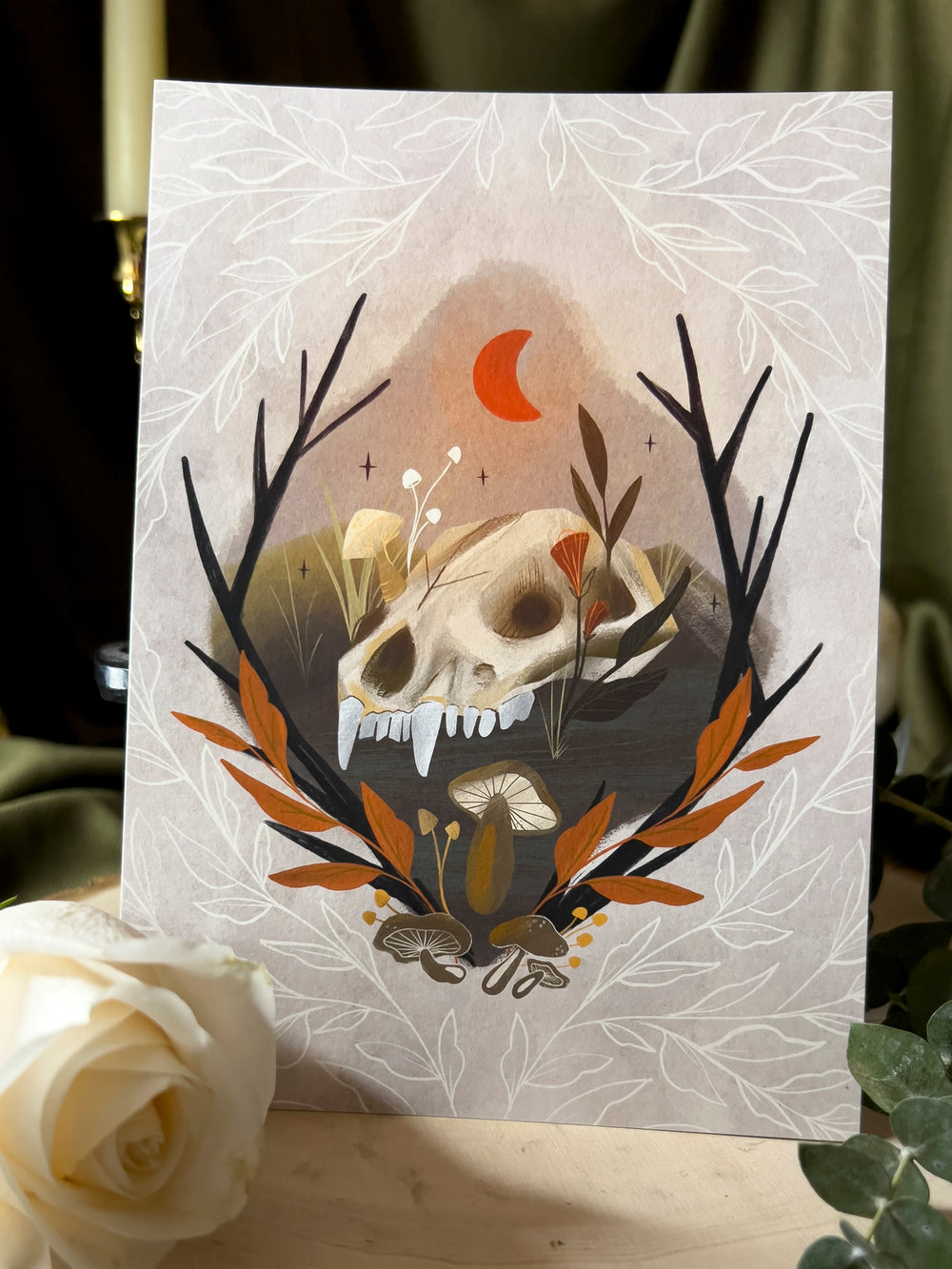 An art print depicting an animal skull on the ground beneath a red crescent moon.
