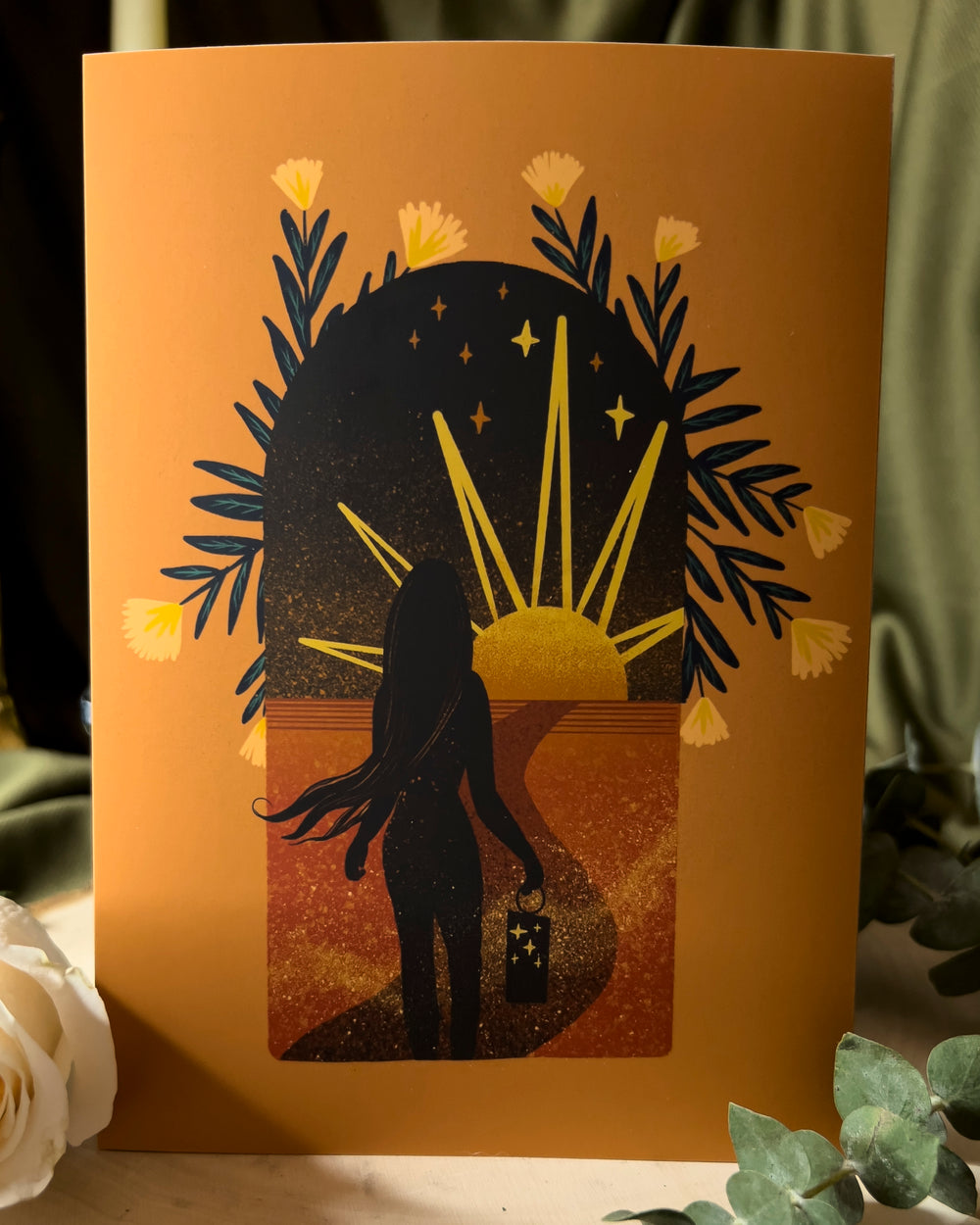 An art print depicting a traveler walking through the desert towards a setting sun with a lantern in their hand.