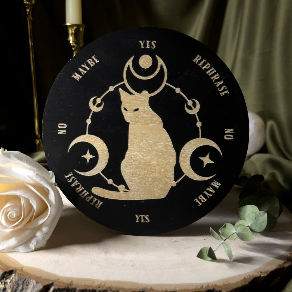 Pendulum board with yes, no, maybe, and rephrase on the edge of the circular board and in the center a cat with moons around them.