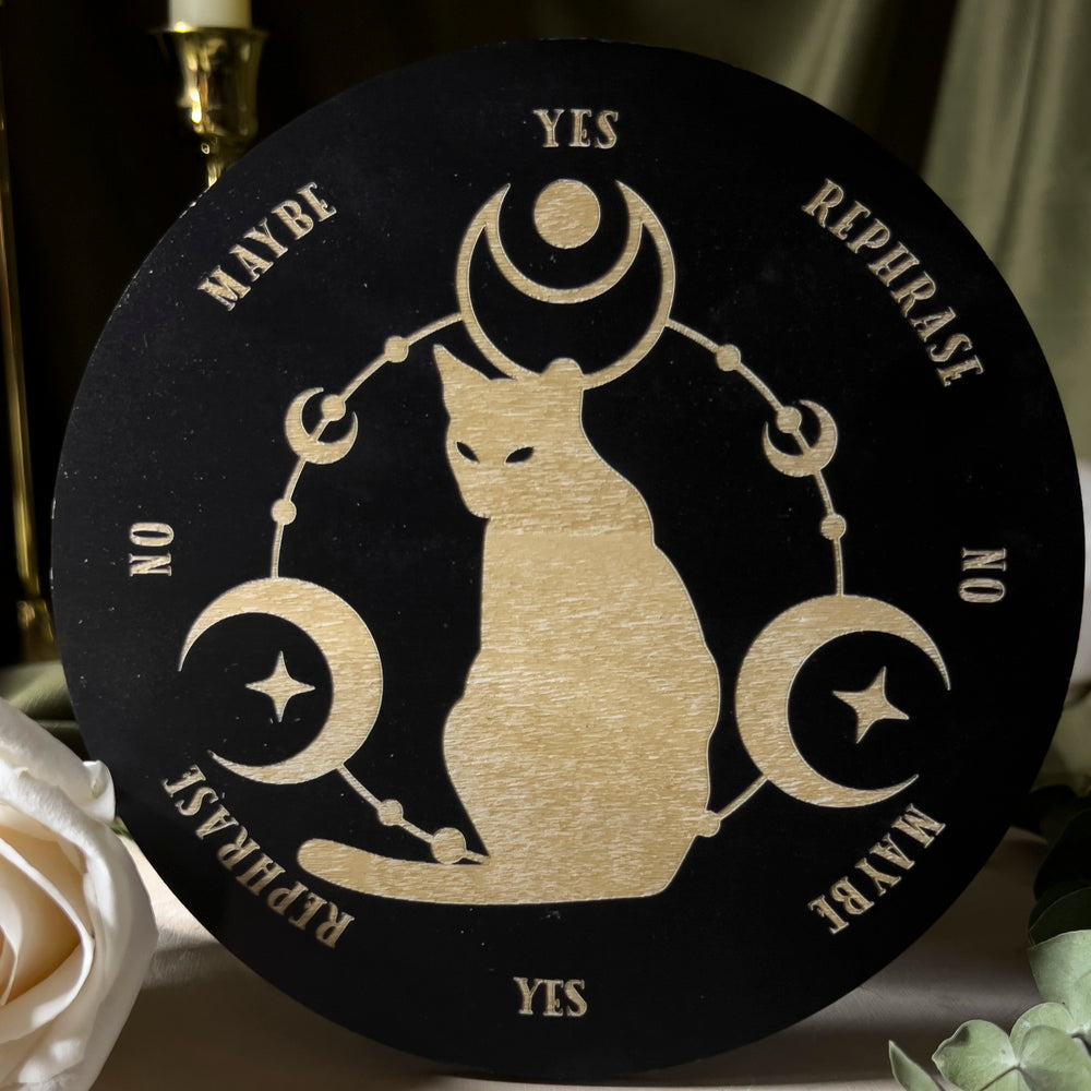 Pendulum board with yes, no, maybe, and rephrase on the edge of the circular board and in the center a cat with moons around them.