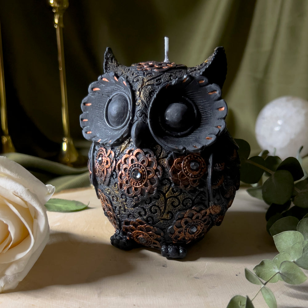 Black owl statue candle with gold floral designs and decorated with rhinestones, close up.