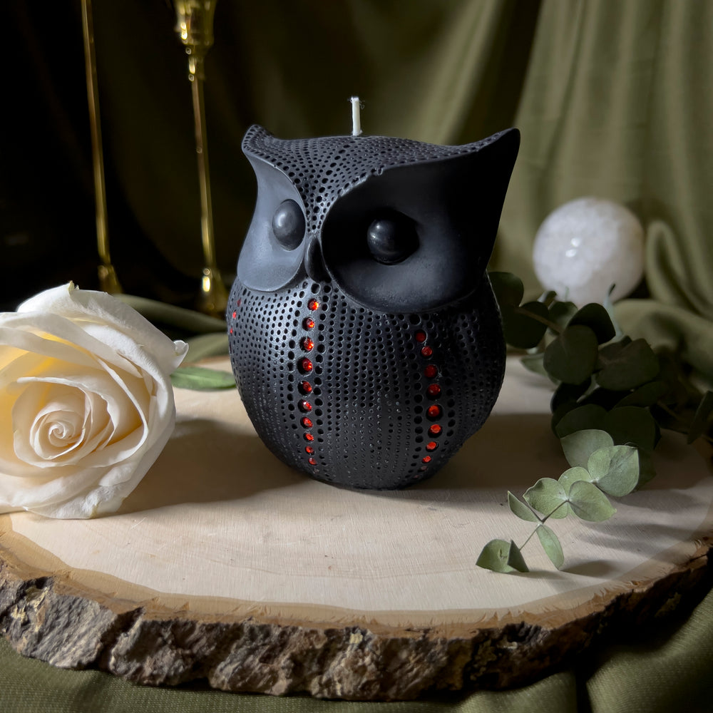 Black owl statue candle with red rhinestones trailing up the sides and front in a single row.