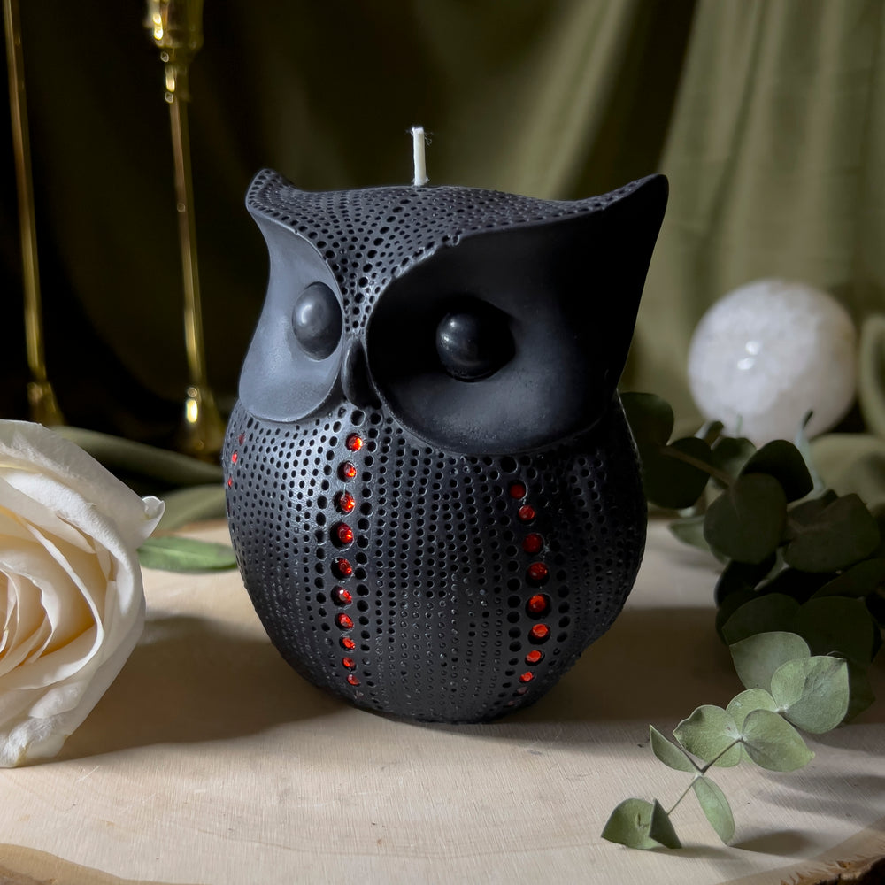 Black owl statue candle with red rhinestones trailing up the sides and front in a single row, close up.