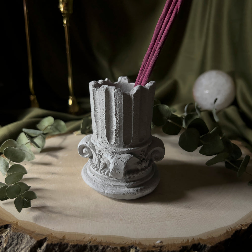 Grey holder shaped like half of a greek column, holding incense as an example.