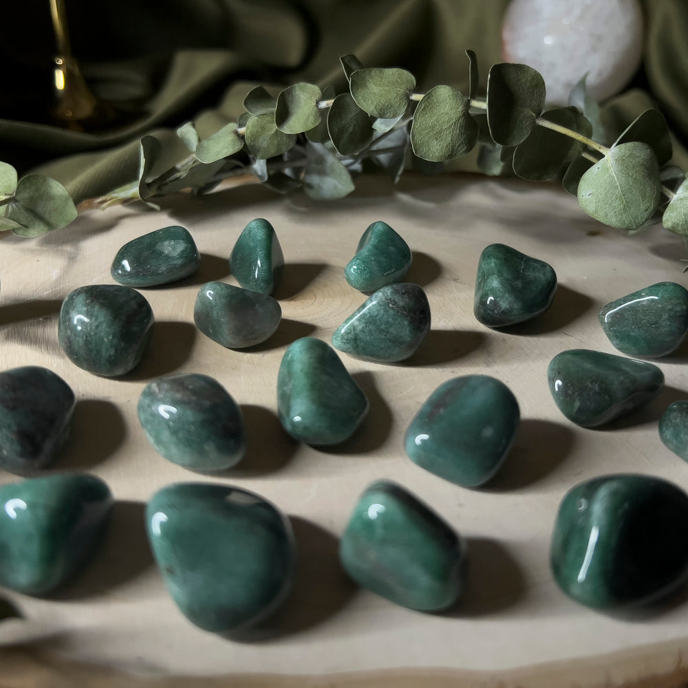 Multiple Deep Green Aventurine Tumbles on wood slice display, closeup.