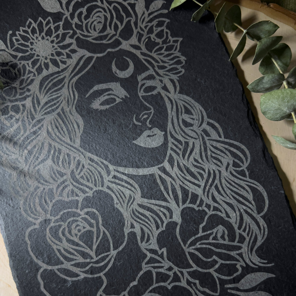 A slate portrait of the goddess Aphrodite with flowers all around her.