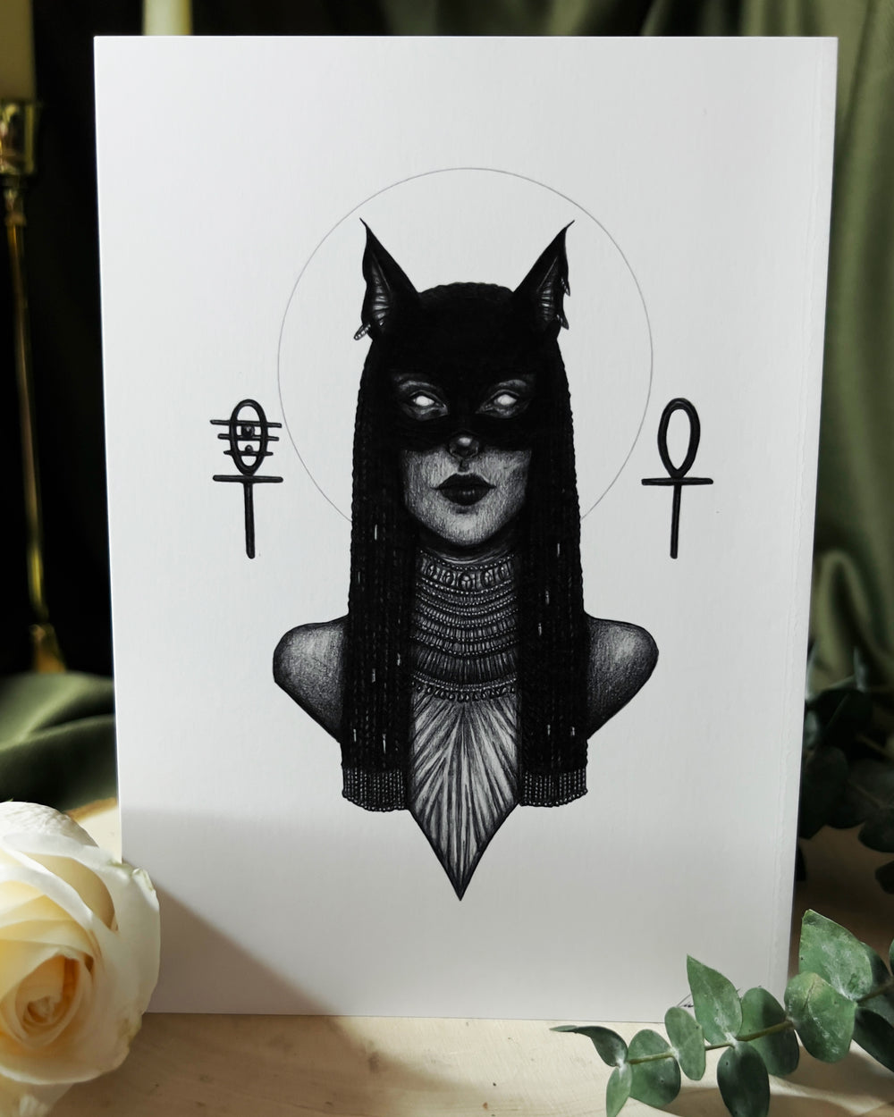 Art print depicting the goddess Bastet with a cat mask covering her eyes and beads around her neck.